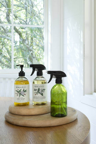 Koala Eco products displayed on a wooden tray, including recycled glass spray bottles and refillable cleaning solutions.