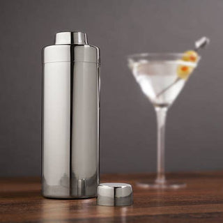 Polished stainless steel cocktail shaker next to a martini glass on a wooden surface, highlighting elegant design.