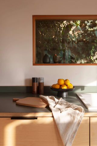 Matte black ceramic footed bowl filled with fresh lemons on a kitchen countertop with wooden accents.