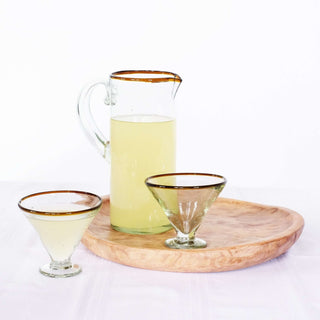Amber rim margarita glasses with a pitcher on a wooden tray, showcasing sustainable, hand-blown glassware for festive occasions.