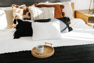 Braided pom pom lumbar pillow on a bed with decorative pillows and a tray, showcasing stylish home decor.