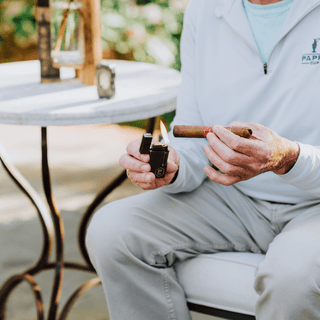 Person lighting a cigar with a custom Colibri Julius lighter outdoors, showcasing a moment of luxury and relaxation.