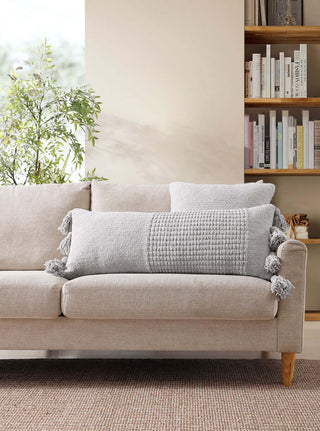 Braided Pom Pom Lumbar Pillow on a beige sofa, featuring a cozy memory foam design with removable cover and stylish pom poms.