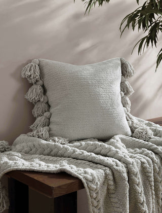 Soft microfiber pom pom throw pillow with textured design, complemented by a cozy knit blanket in a serene setting.