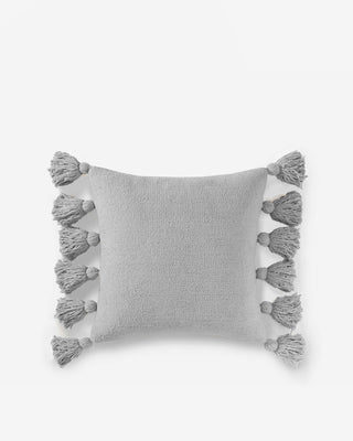 Light gray pom pom throw pillow with soft microfiber and fuzzy tassels on edges, perfect for cozy decor.