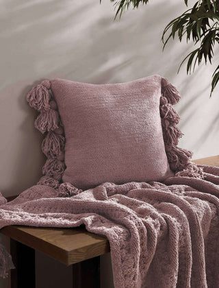 Soft microfiber pom pom throw pillow in blush pink, paired with a cozy blanket on a wooden surface.