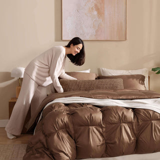 Woman arranging a bed with Premium Bamboo Bubble Comforter and matching pillows in a cozy bedroom setting.