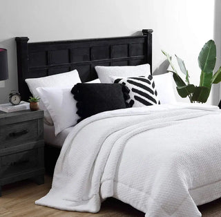 Cozy bedroom with a white quilt, decorative pillows including a pom pom throw pillow, and a black wooden headboard.