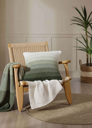 Ombre throw pillow in shades of green and cream placed on a chair with a cozy blanket, enhancing a contemporary living space.