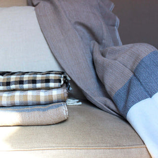 Bina Brown Throw Blanket draped over a couch with folded plaid and patterned blankets for cozy living space decor.