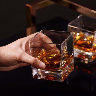 Hand holding a Braque crystal rocks glass filled with whiskey, showcasing its modern square design.