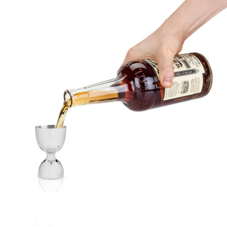 Bartender pouring liquor from a bottle into a stainless steel double jigger for cocktail mixing.