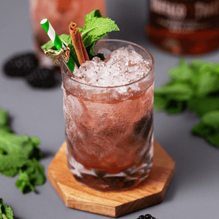 Delicious cocktail in crystal tumbler, garnished with mint, cinnamon stick, and served over crushed ice.