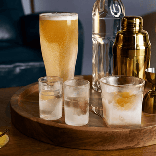 Elegant whiskey glasses on a wooden tray with beer and cocktail shaker, showcasing refreshing drink options for any occasion.