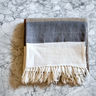 Bina Brown Throw Blanket, hand-loomed merino wool with unique design, folded on marble surface.