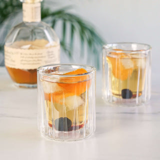Double-walled rocks glasses set of 2 with cocktails and garnishes on a marble surface.